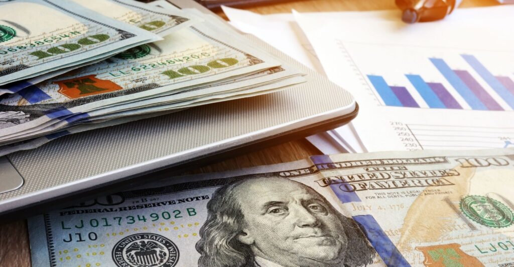 $100 bills next to laptop and graph