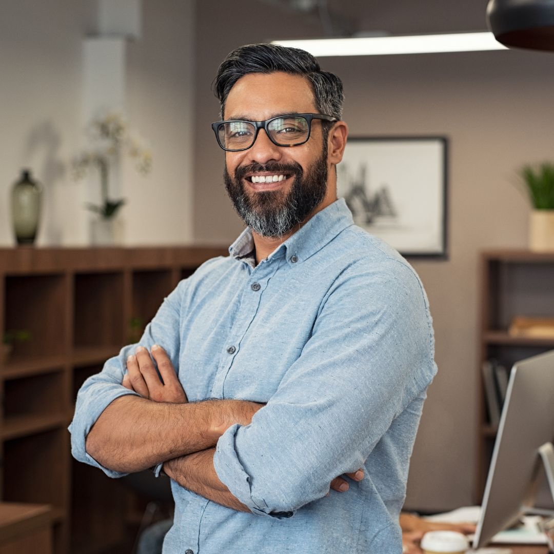 Man in blue button up shirt smiling while leaning on his desk