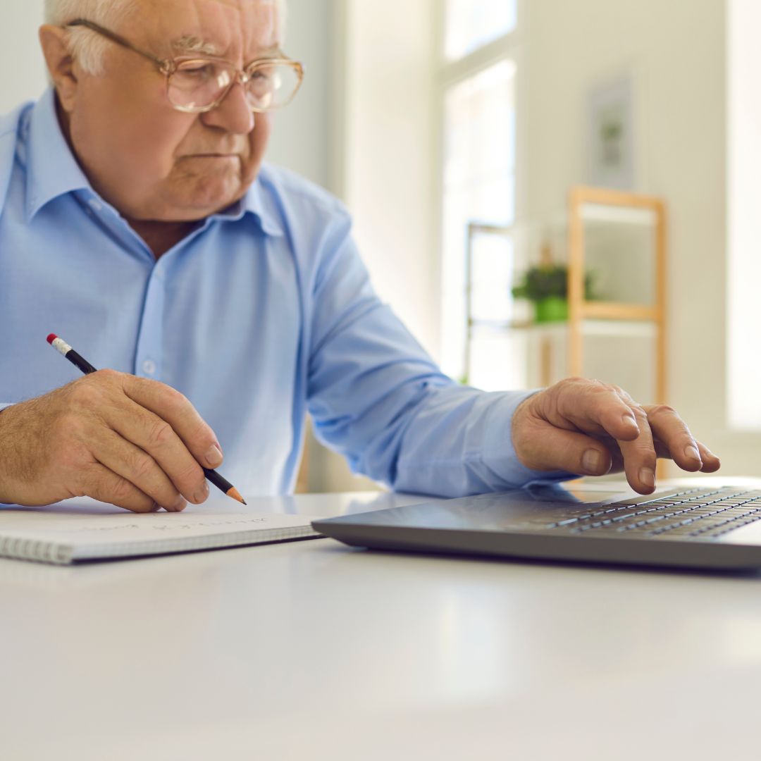 an older man looking at a computer and taking notes