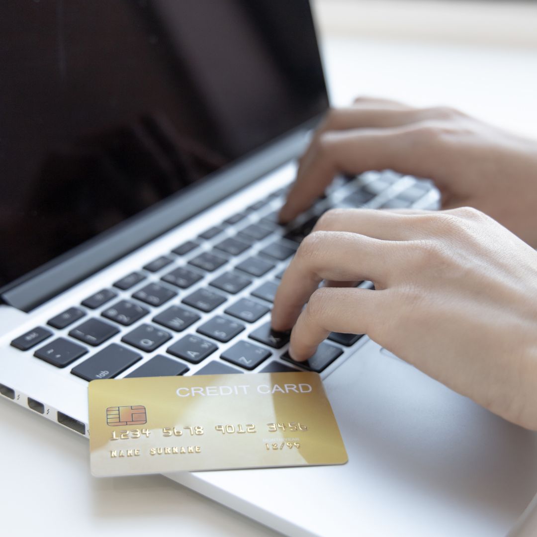 a person typing on a laptop with a credit card nearby