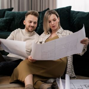 man and woman sit on floor looking at architectural drawings together