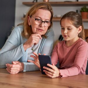 older woman looks at screen while sitting next to girl holding phone 