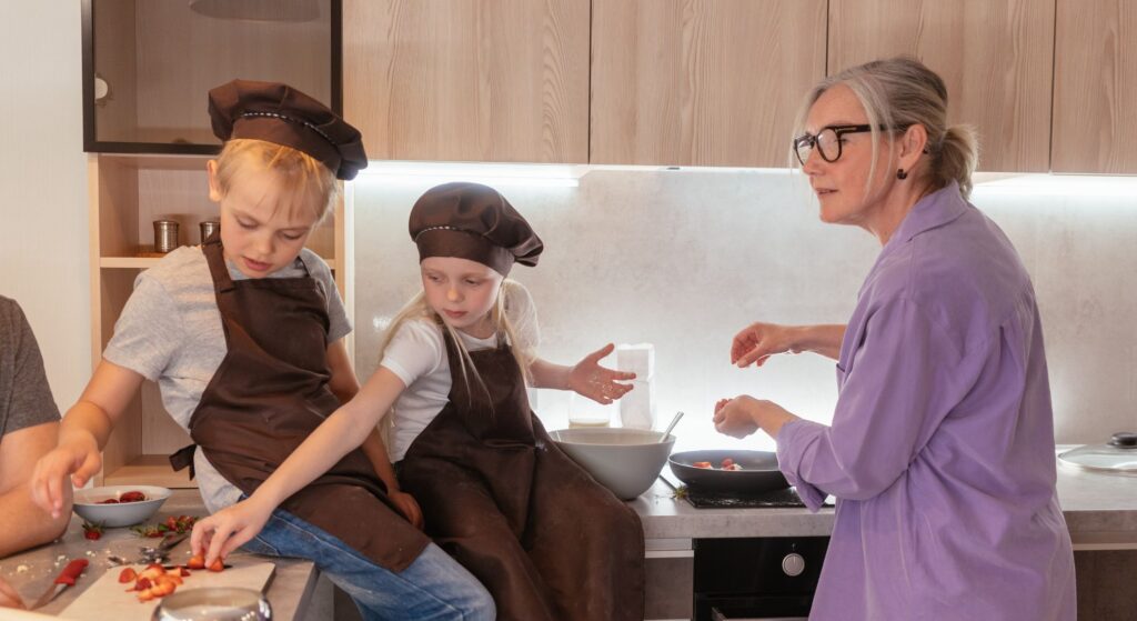 woman cooks while grandkids snack on strawberries