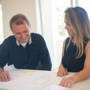 man looks at blueprint on table sitting next to woman smiling