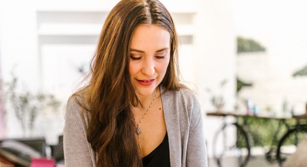 woman with long hair smiles while looking down at what she is holding