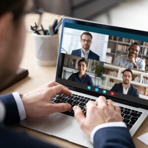 person sits at laptop with faces of people on video call 