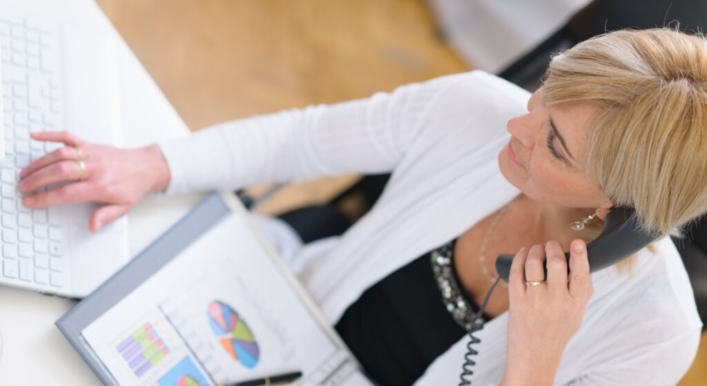 woman holds phone to her ear while sitting at desk