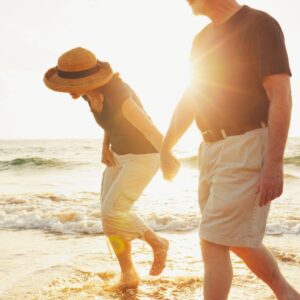 man and woman wearing khaki shorts and hats walk on beach at sunset